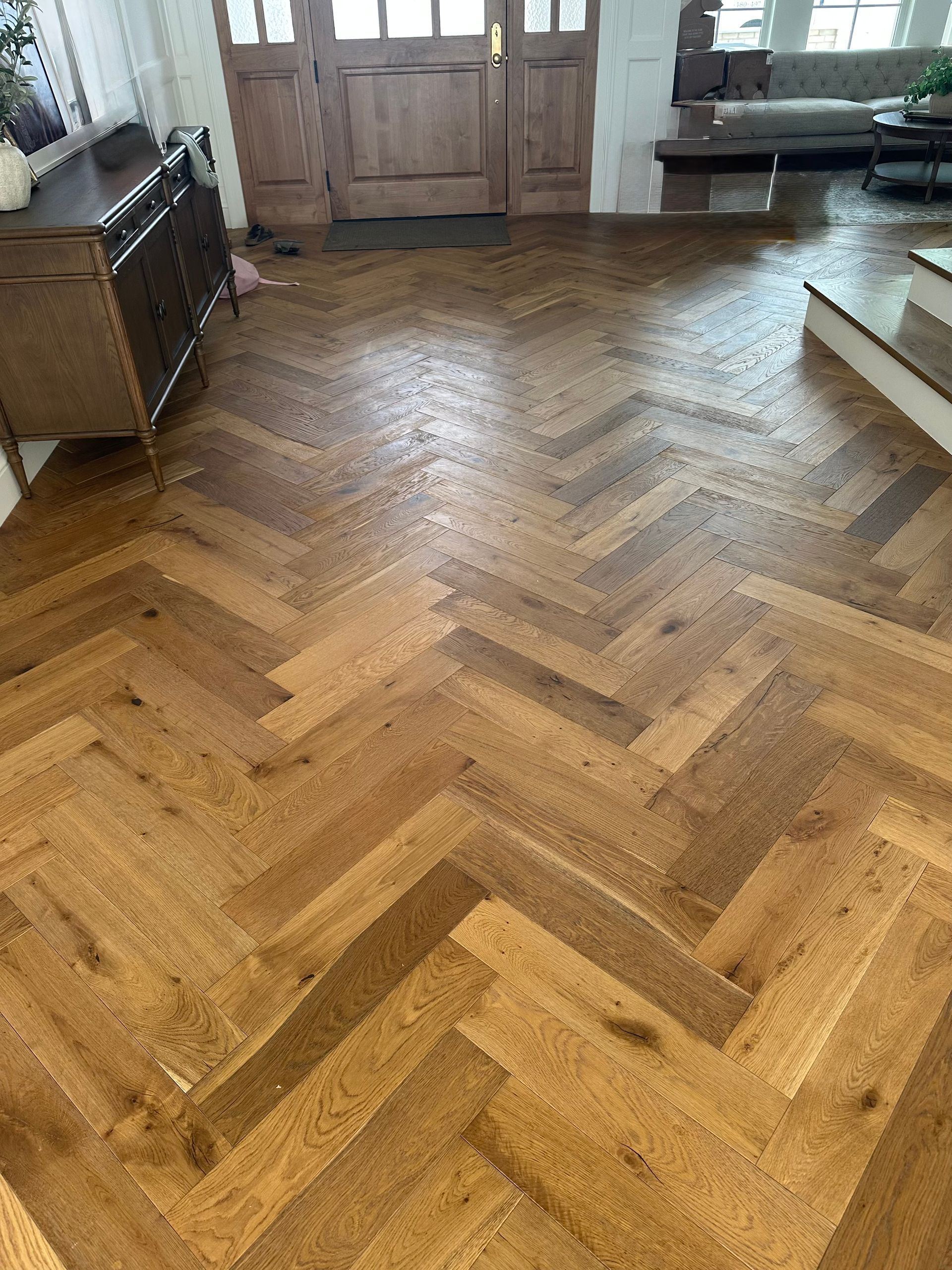 Wooden herringbone floor in a living room with a front door and furniture visible.