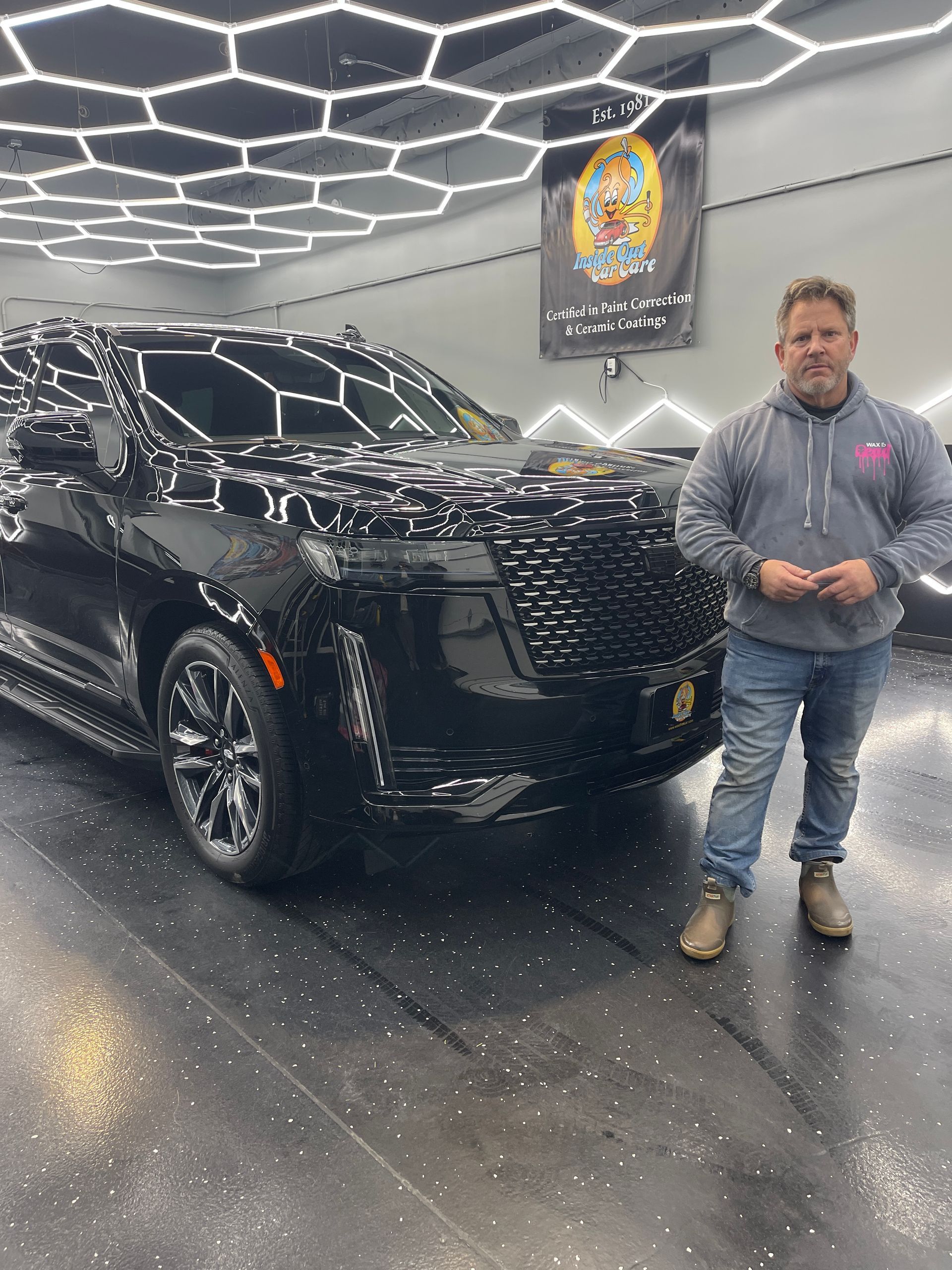 A man is standing in front of a black suv in a garage.