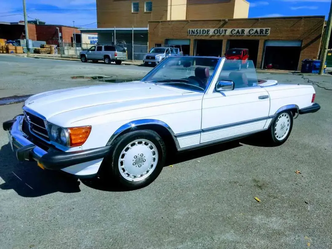 A white convertible is parked in front of a car dealership