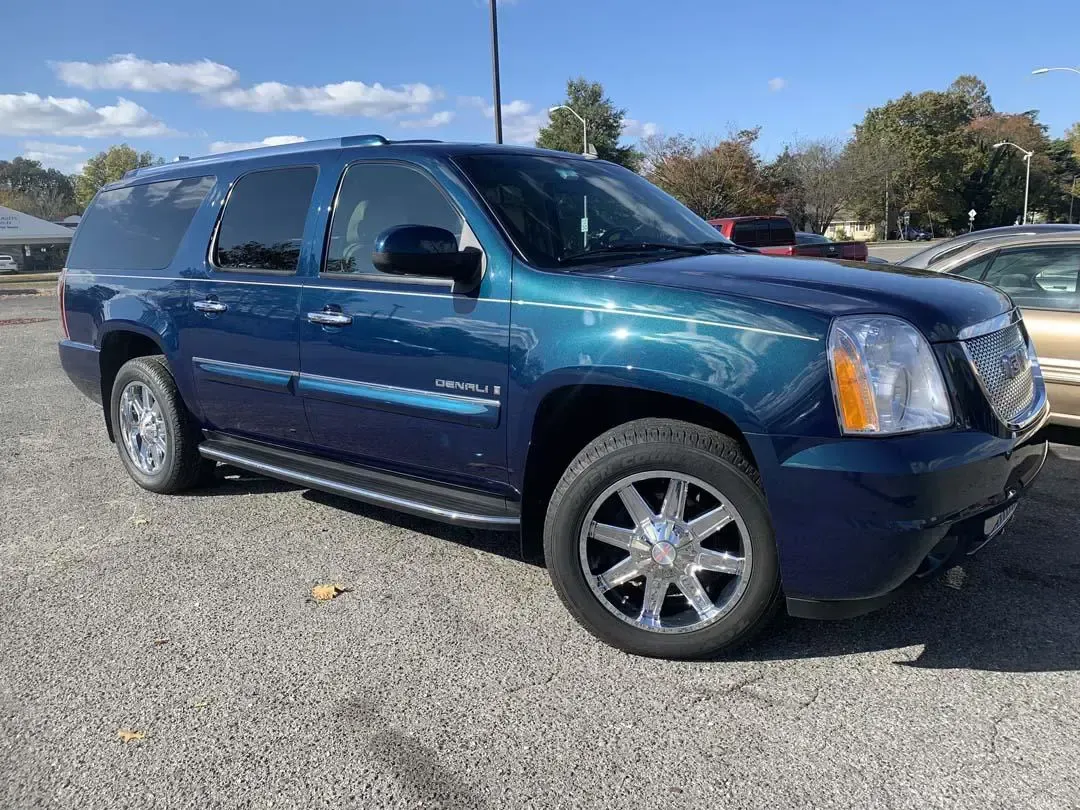 A blue gmc yukon is parked in a gravel lot.