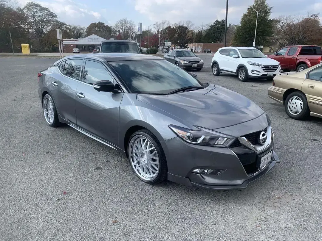 A gray nissan maxima is parked in a parking lot.