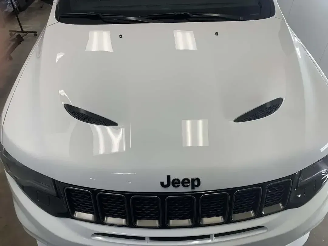 A white jeep is parked in a garage with the hood up.