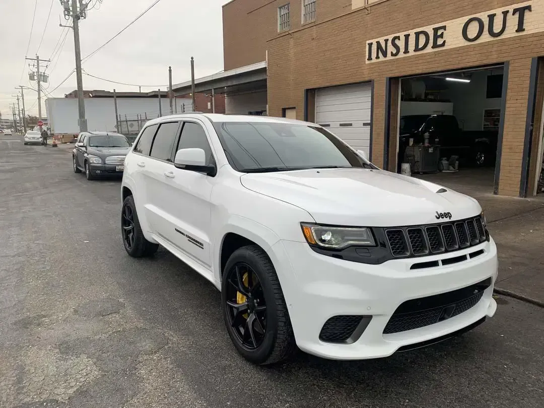 A white jeep grand cherokee is parked in front of a garage.