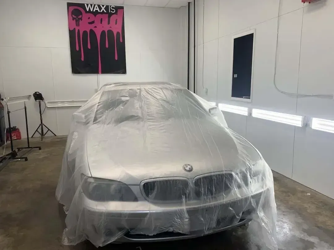 A silver car is covered in plastic in a garage.