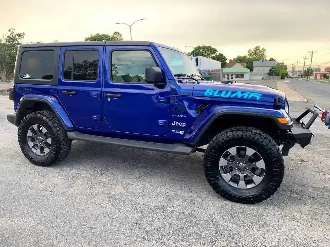 A blue jeep wrangler is parked in a gravel lot.