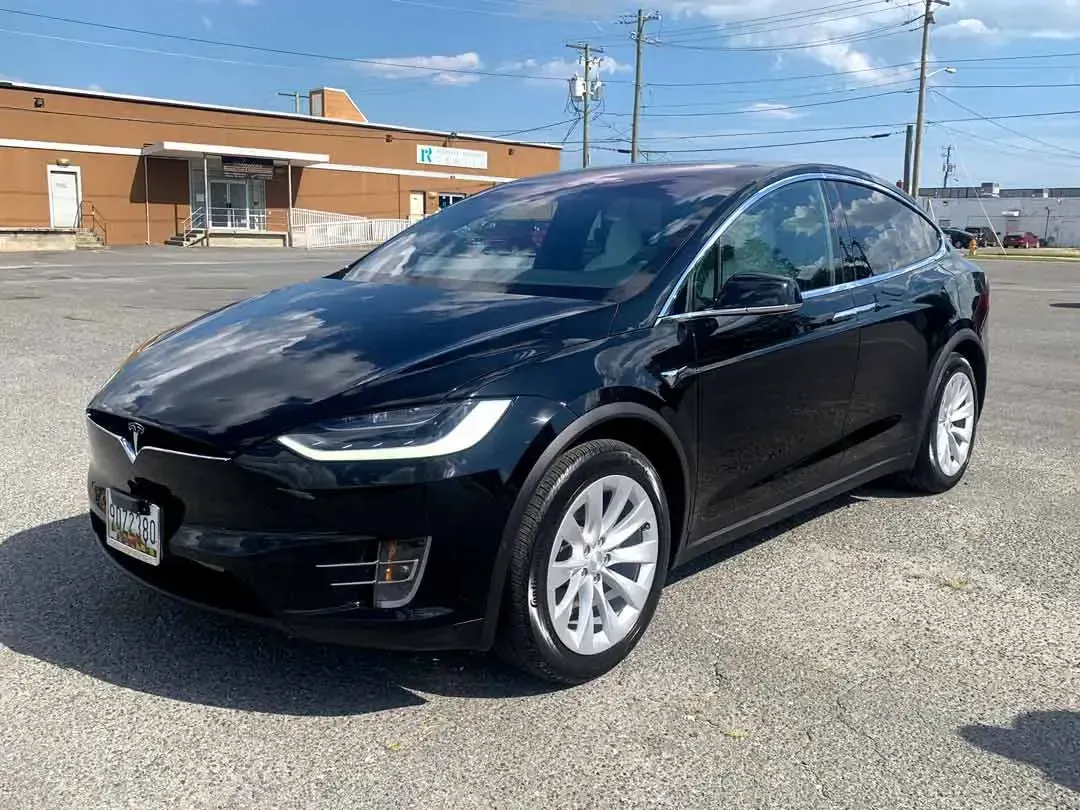 A black tesla model x is parked in a parking lot in front of a building.