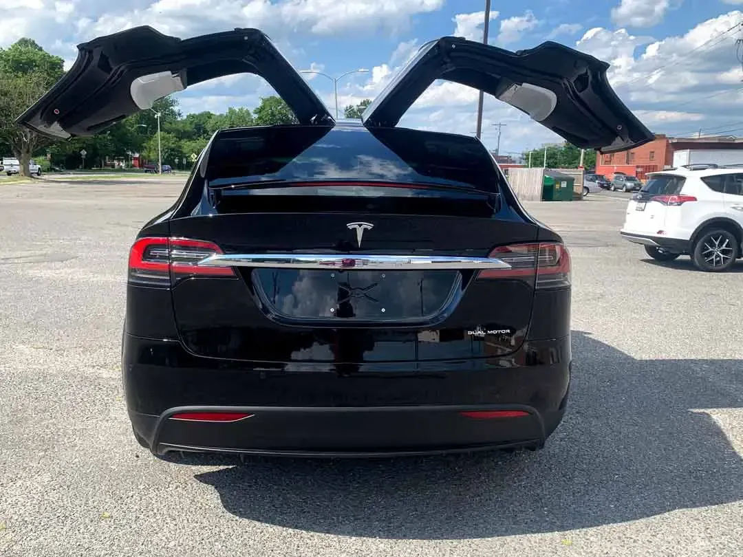 A black tesla model x with its doors open is parked in a parking lot.