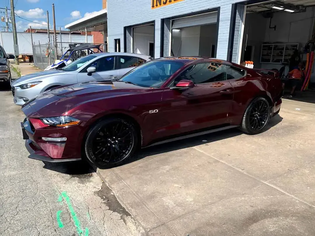A red ford mustang is parked in front of a garage.