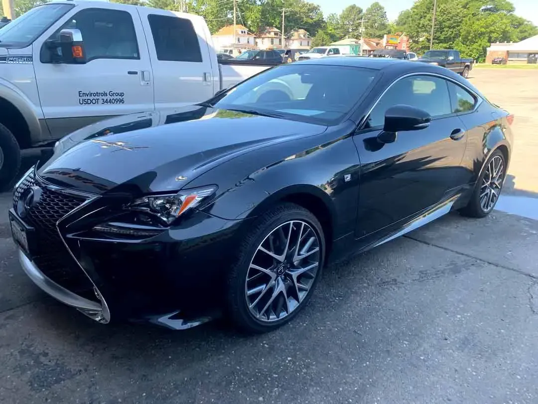 A black lexus rc is parked in a parking lot next to a white truck.