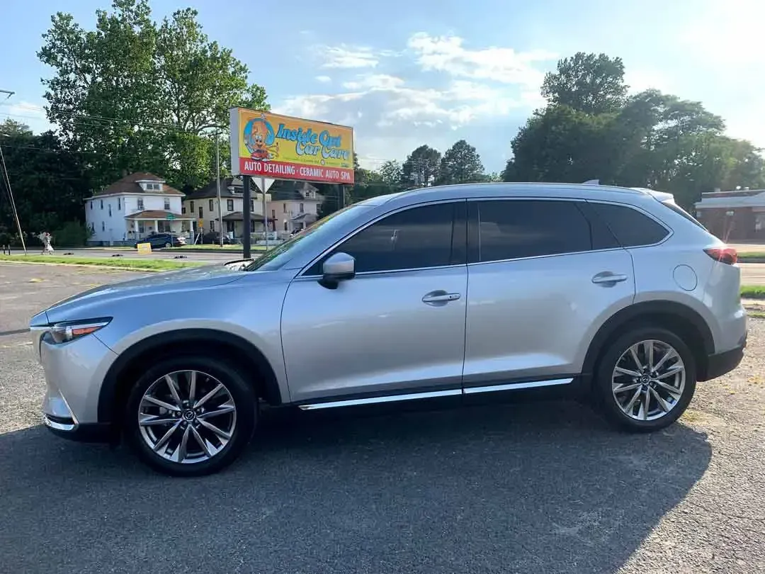 A silver mazda cx 9 is parked in a parking lot in front of a billboard.