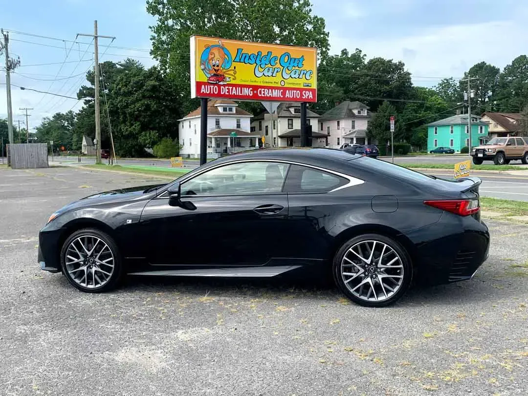 A black car is parked in a parking lot in front of a billboard.
