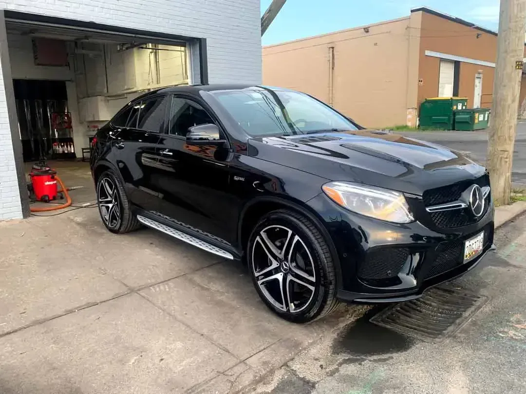 A black mercedes benz gle is parked on the side of the road in front of a garage.
