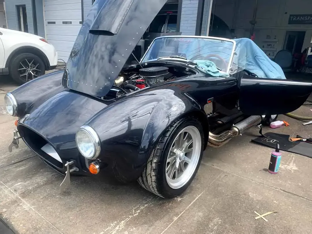 A black sports car with the hood up is parked in front of a garage.