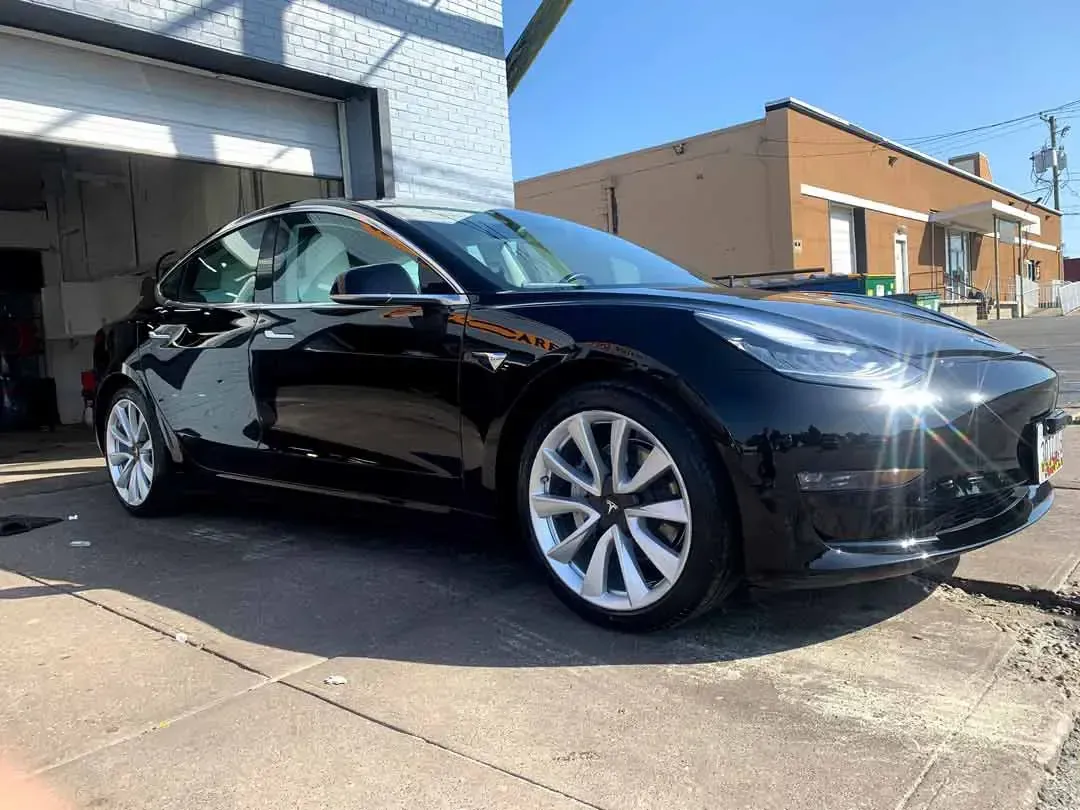 A black tesla model 3 is parked in front of a garage.