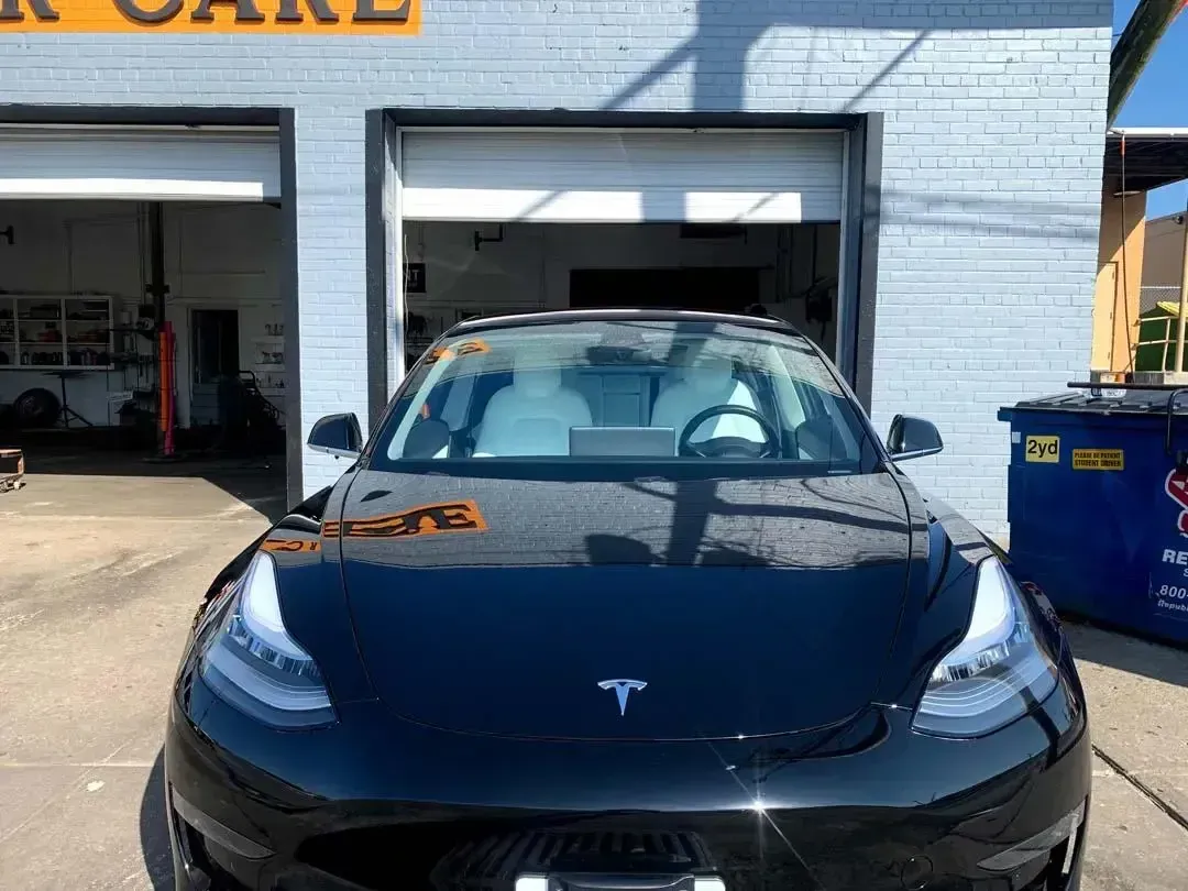 A black tesla model 3 is parked in front of a garage.