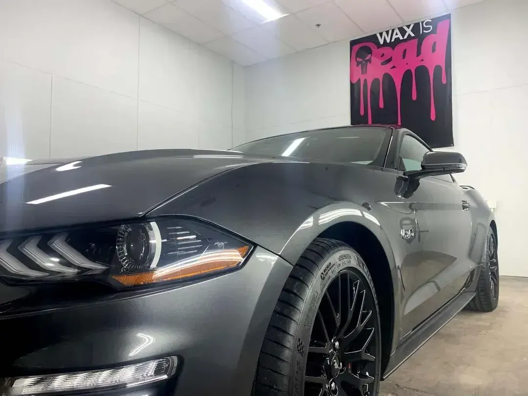 A gray mustang is parked in front of a sign that says wax is.