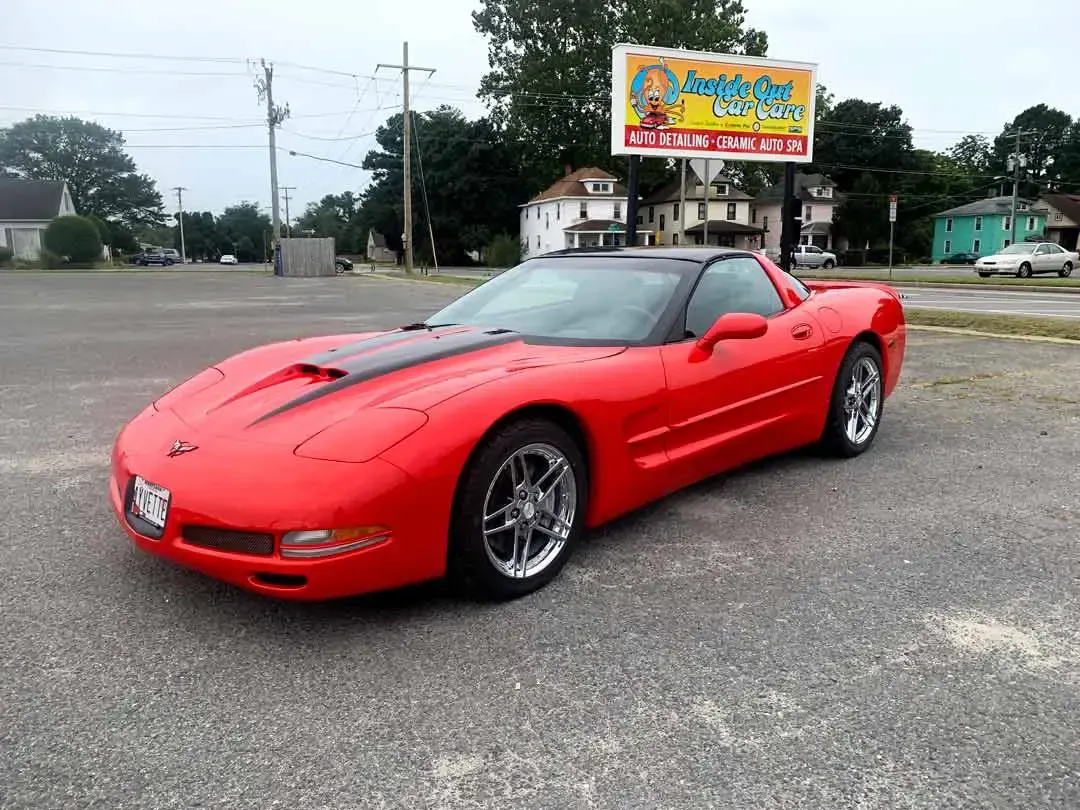 A red corvette is parked in a parking lot in front of a billboard.