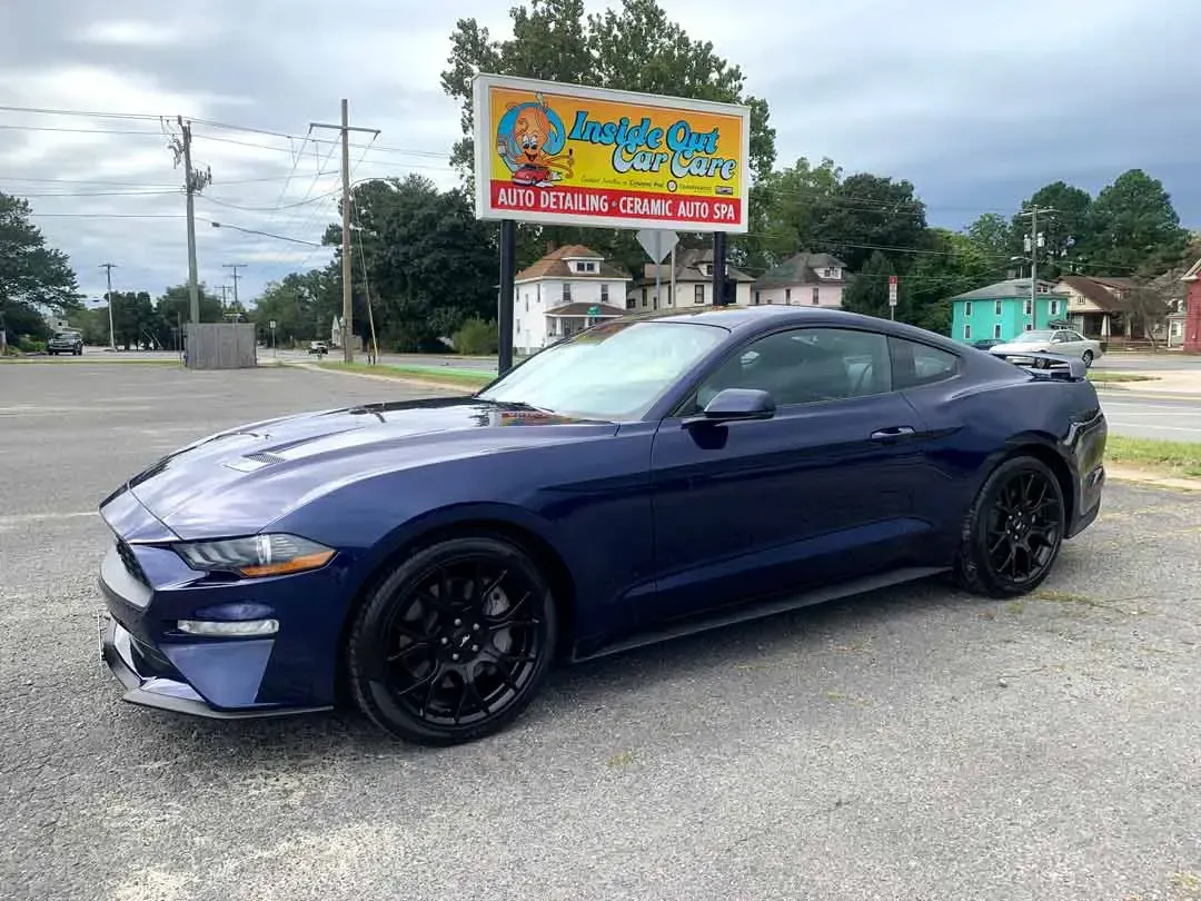A blue ford mustang is parked in front of a billboard.