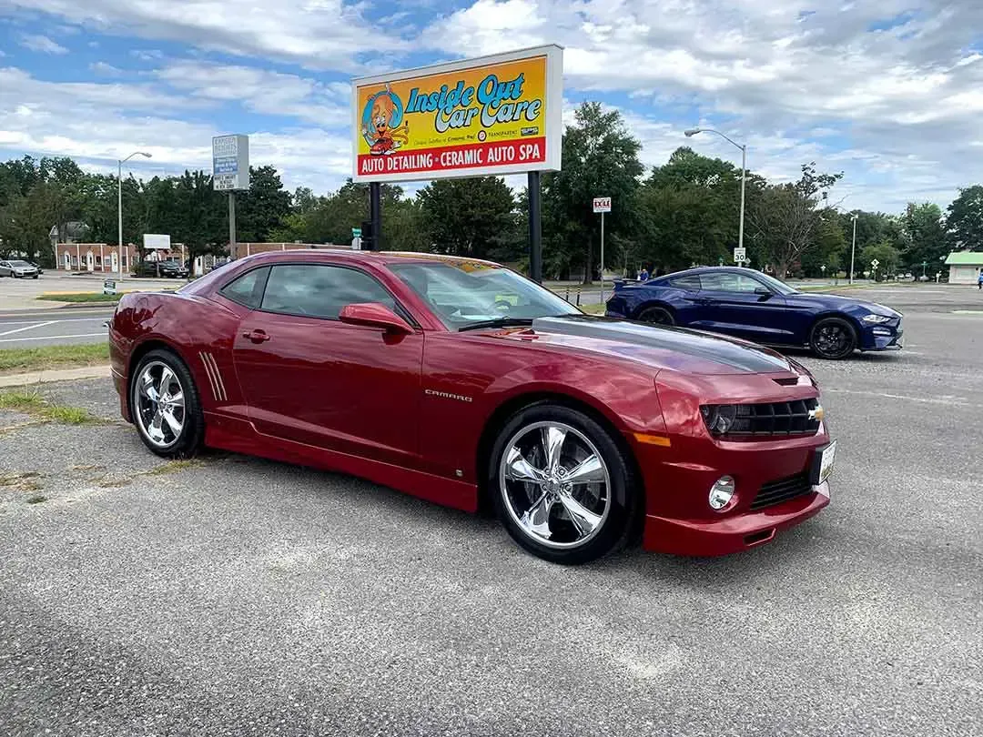 A red car is parked in a parking lot in front of a billboard.