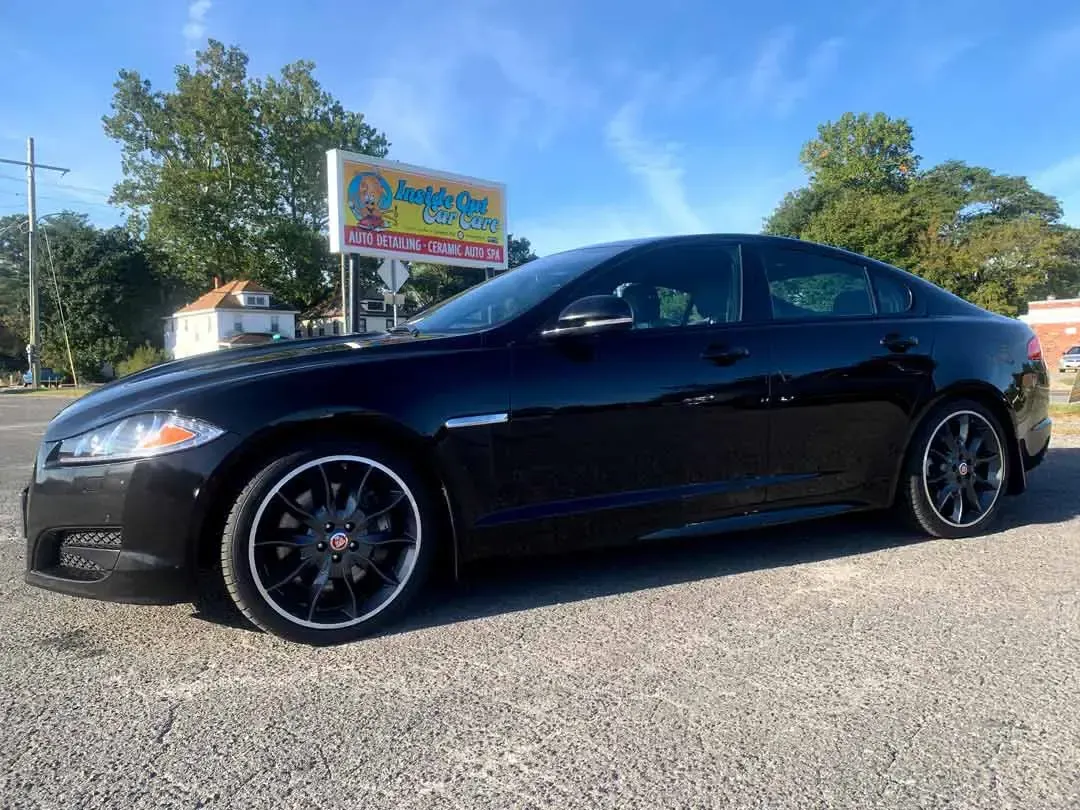 A black jaguar f type is parked in a gravel lot.
