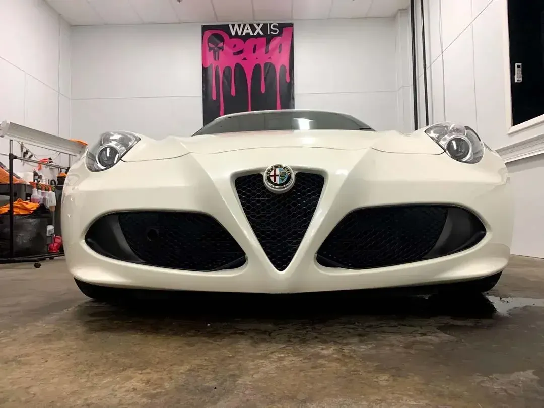 A white alfa romeo 4c4 is parked in a garage.