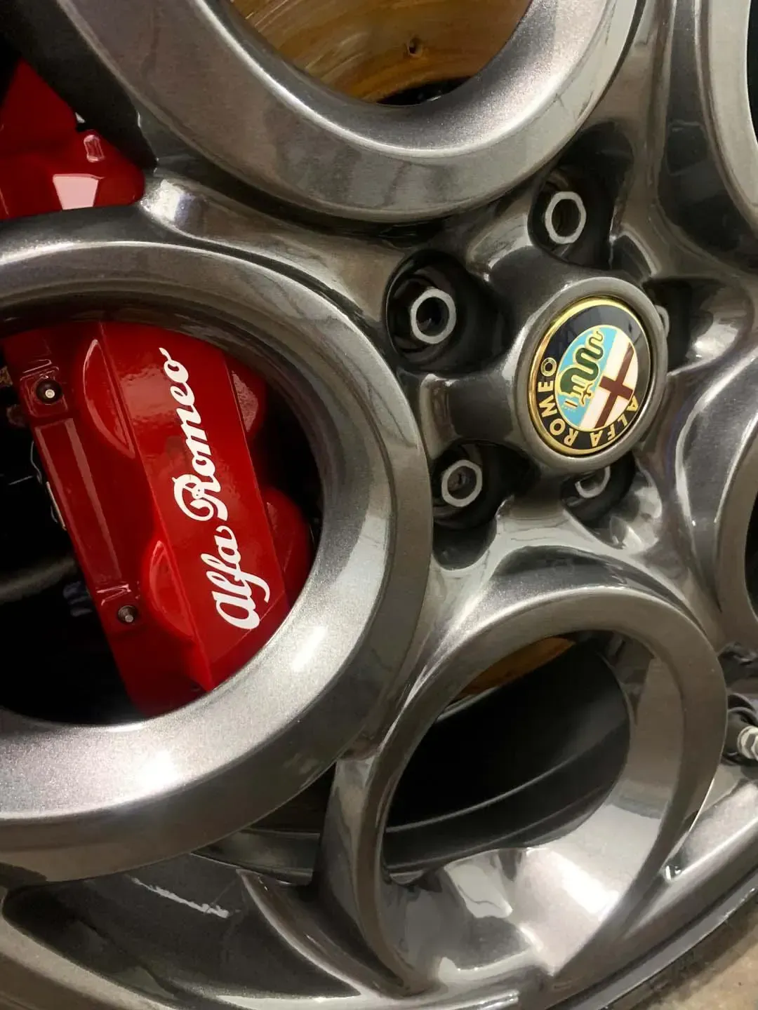 A close up of a red alfa romeo brake caliper on a wheel.