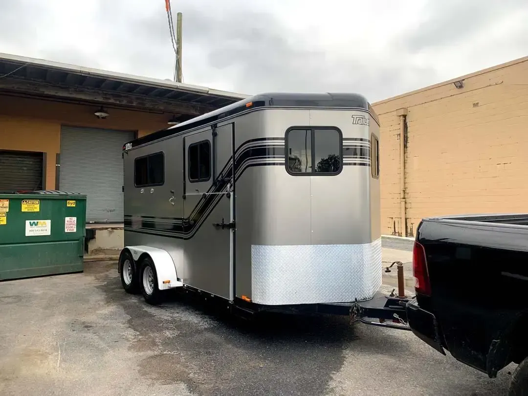 A horse trailer is being towed by a truck in a parking lot.