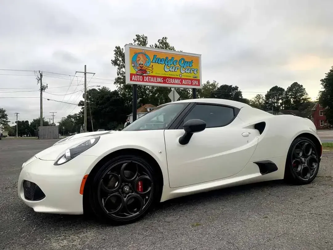 A white sports car is parked in front of a billboard.
