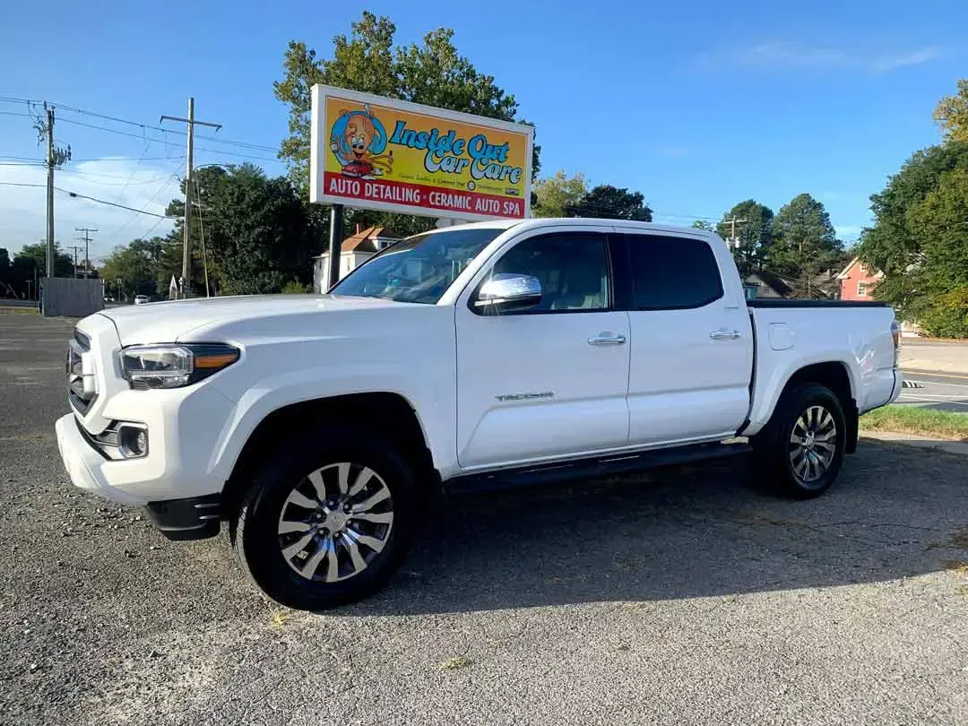 A white toyota tacoma truck is parked in front of a billboard.