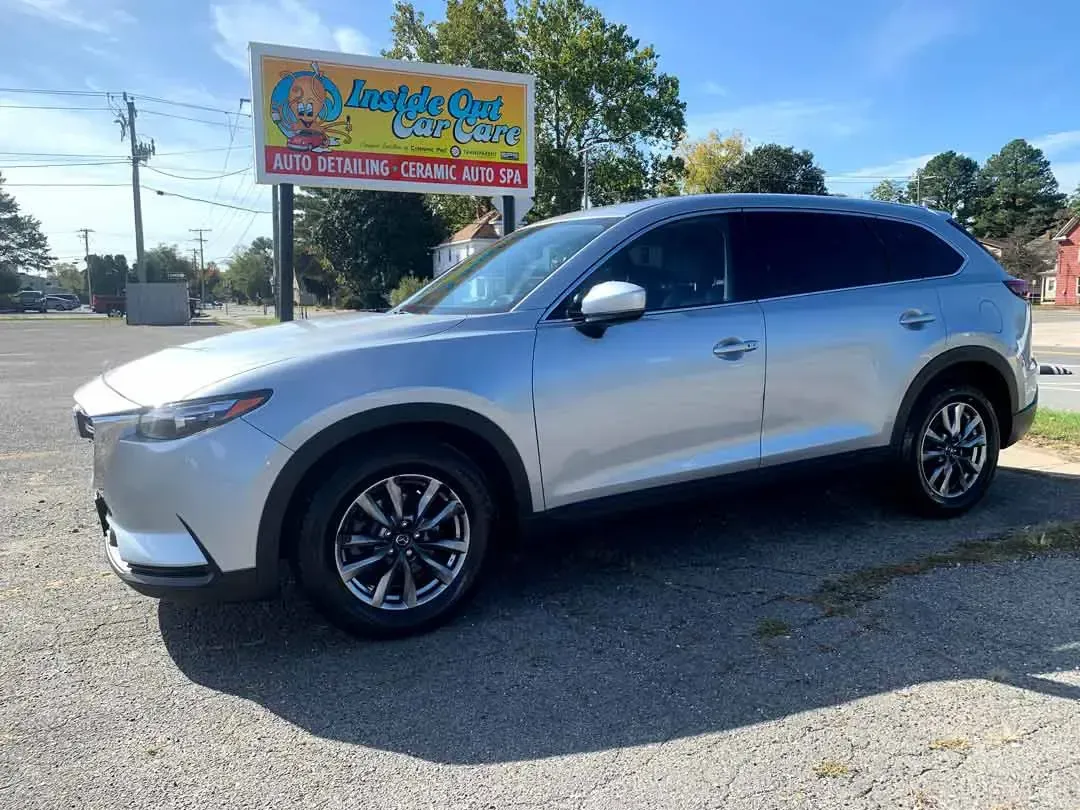 A silver mazda cx 9 is parked in a parking lot next to a sign.