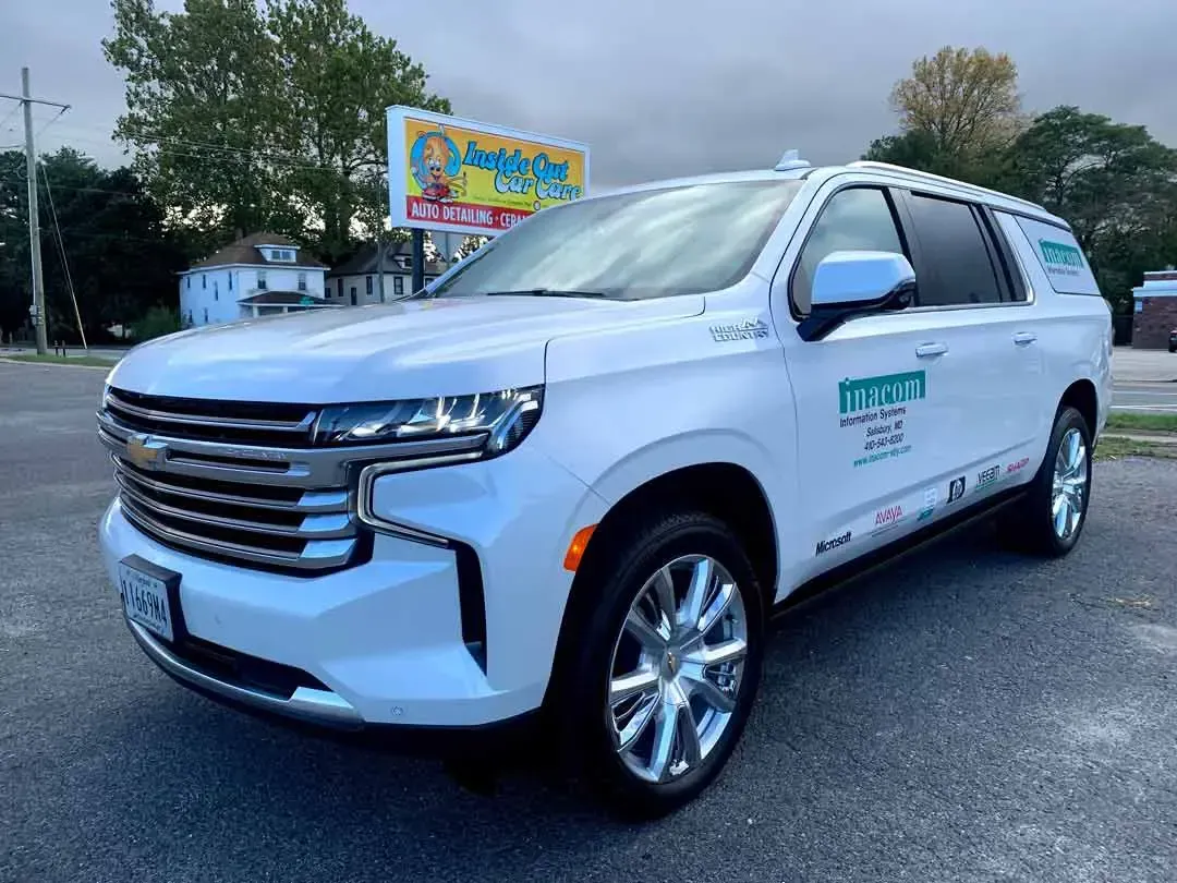 A white suv is parked in a parking lot in front of a billboard.