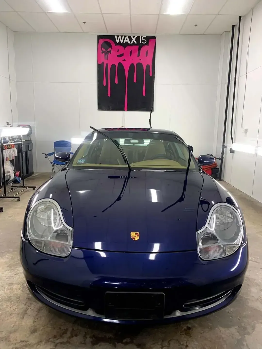 A blue sports car is parked in a garage under a sign that says wax is bad.