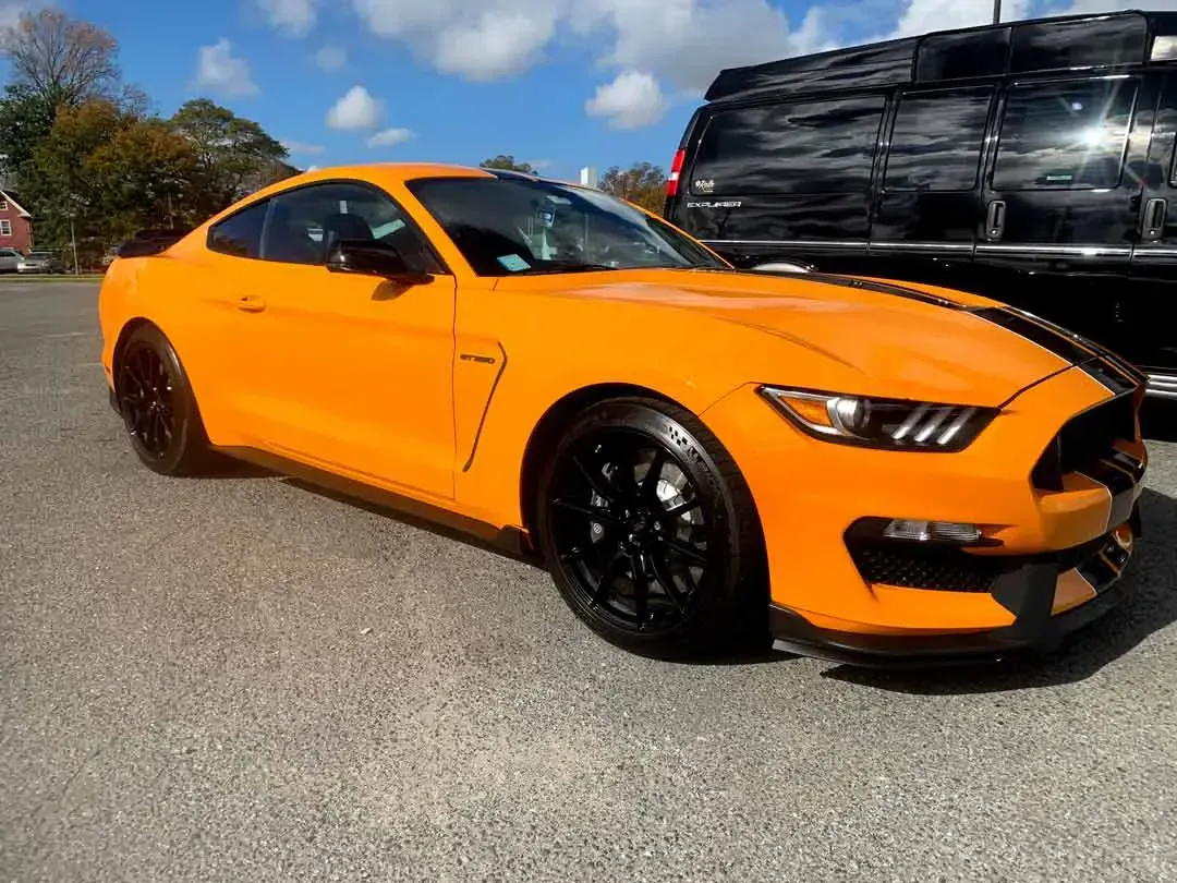 A yellow ford mustang is parked in a parking lot next to a black van.