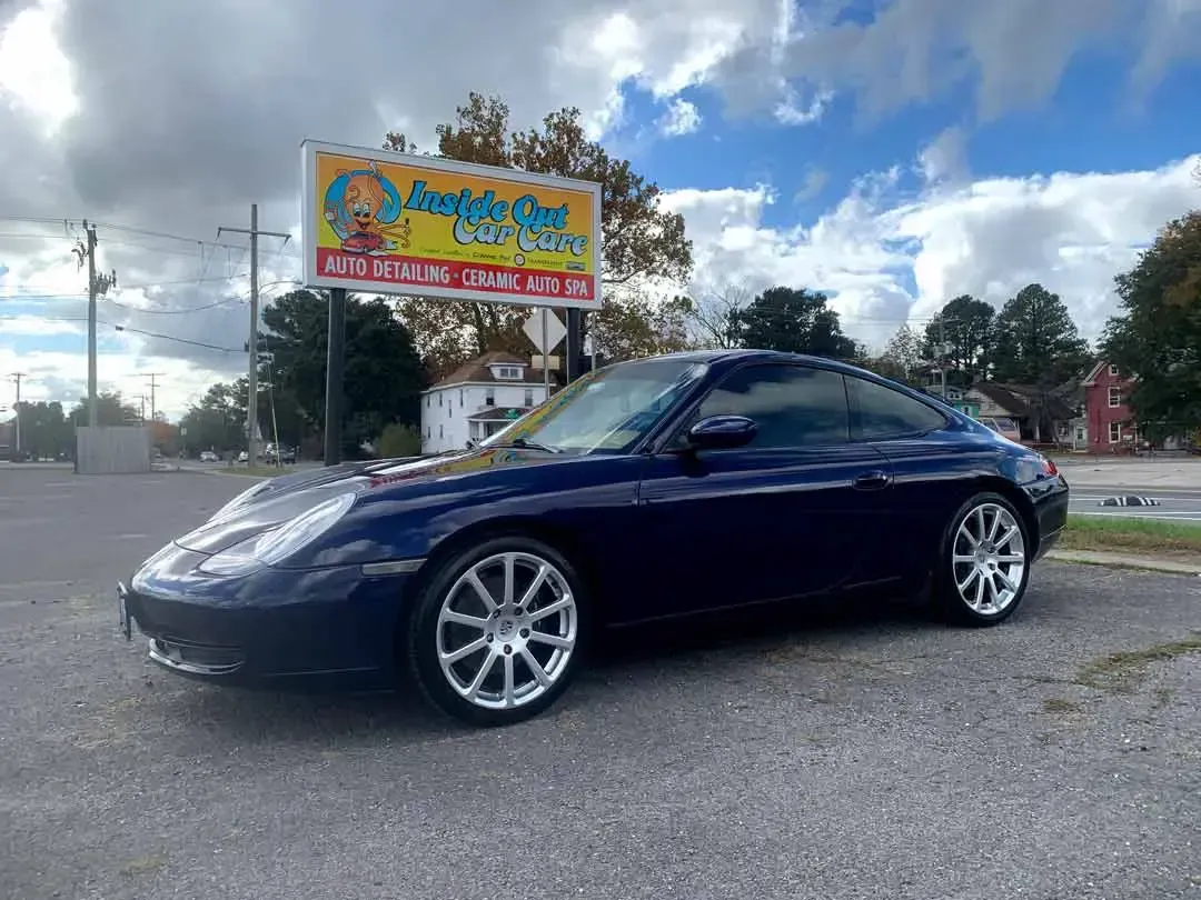 A blue porsche 911 is parked in front of a billboard.
