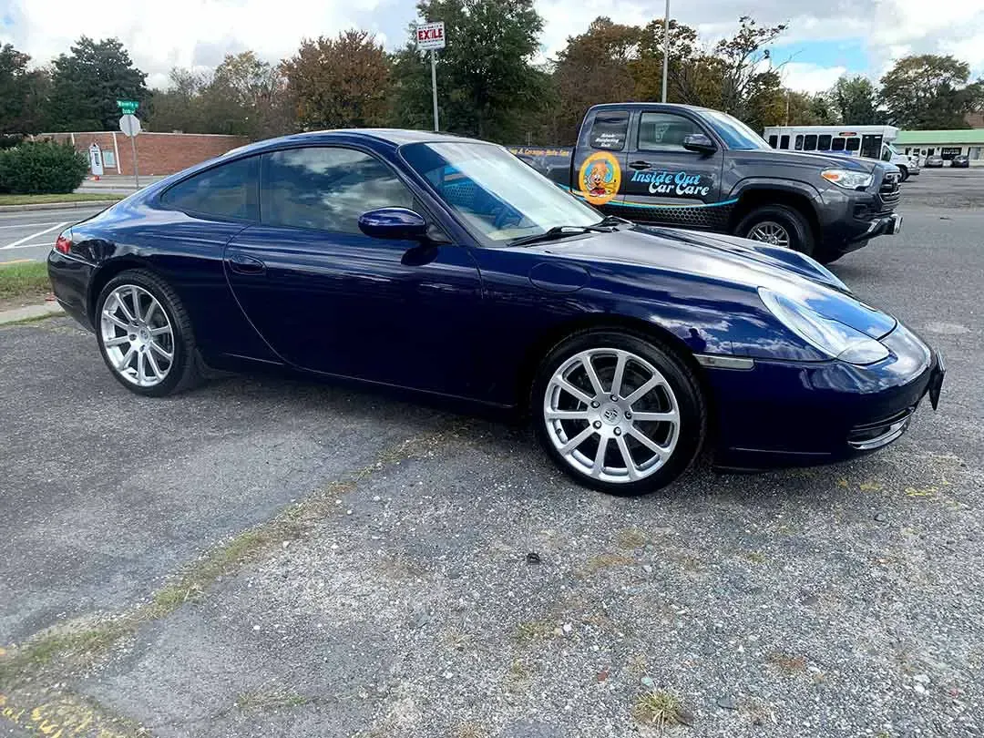 A blue porsche 911 is parked in a parking lot next to a black truck.