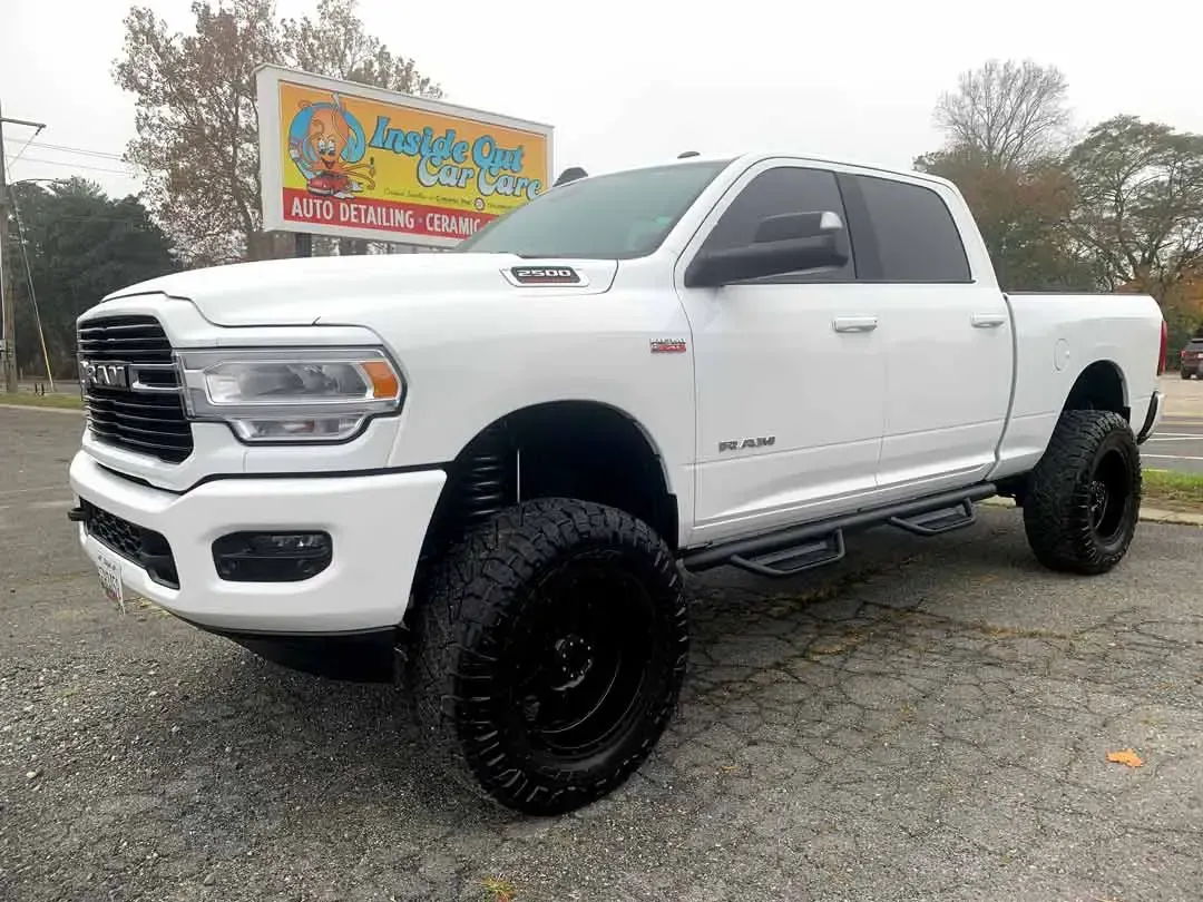 A white ram truck is parked in a parking lot in front of a billboard.