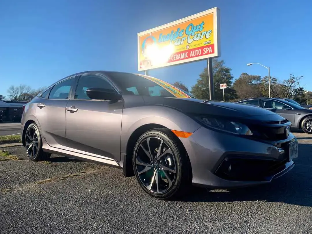 A gray honda civic hatchback is parked in front of a car dealership.