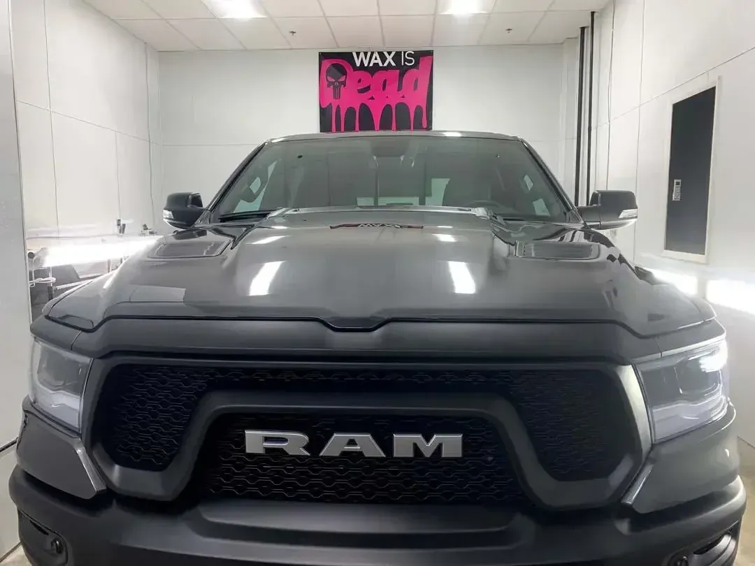 A ram truck is parked in a room with a sign above it that says wax 's