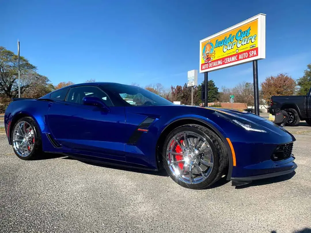 A blue sports car is parked in a gravel lot in front of a sign.