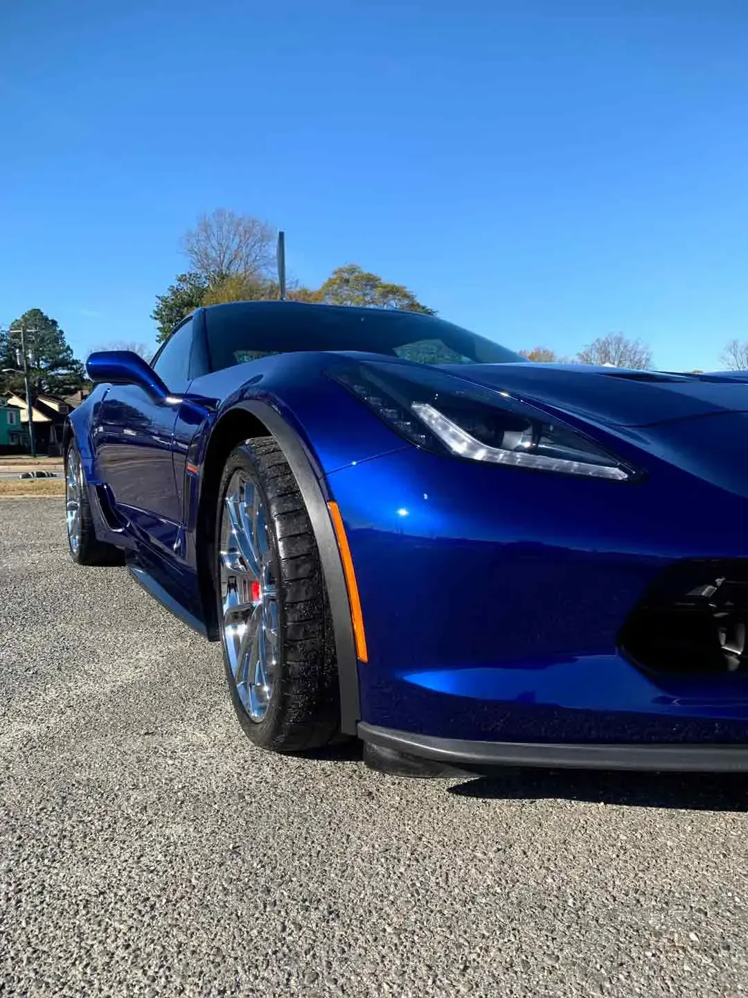 A blue corvette is parked in a gravel lot on a sunny day.