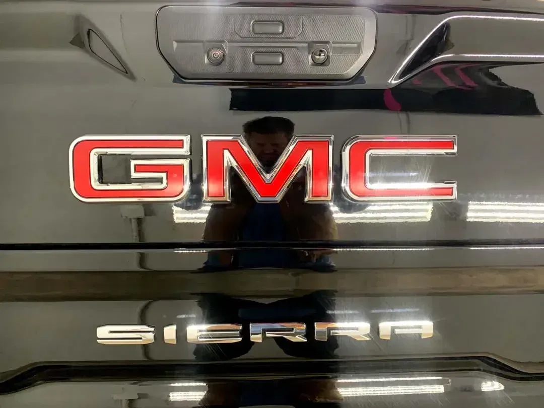 A man is reflected in the back window of a gmc sierra truck.