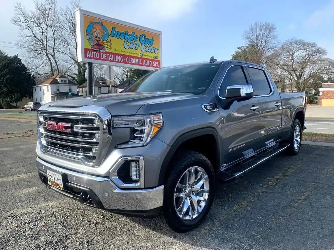 A gray gmc sierra pickup truck is parked in front of a car dealership.