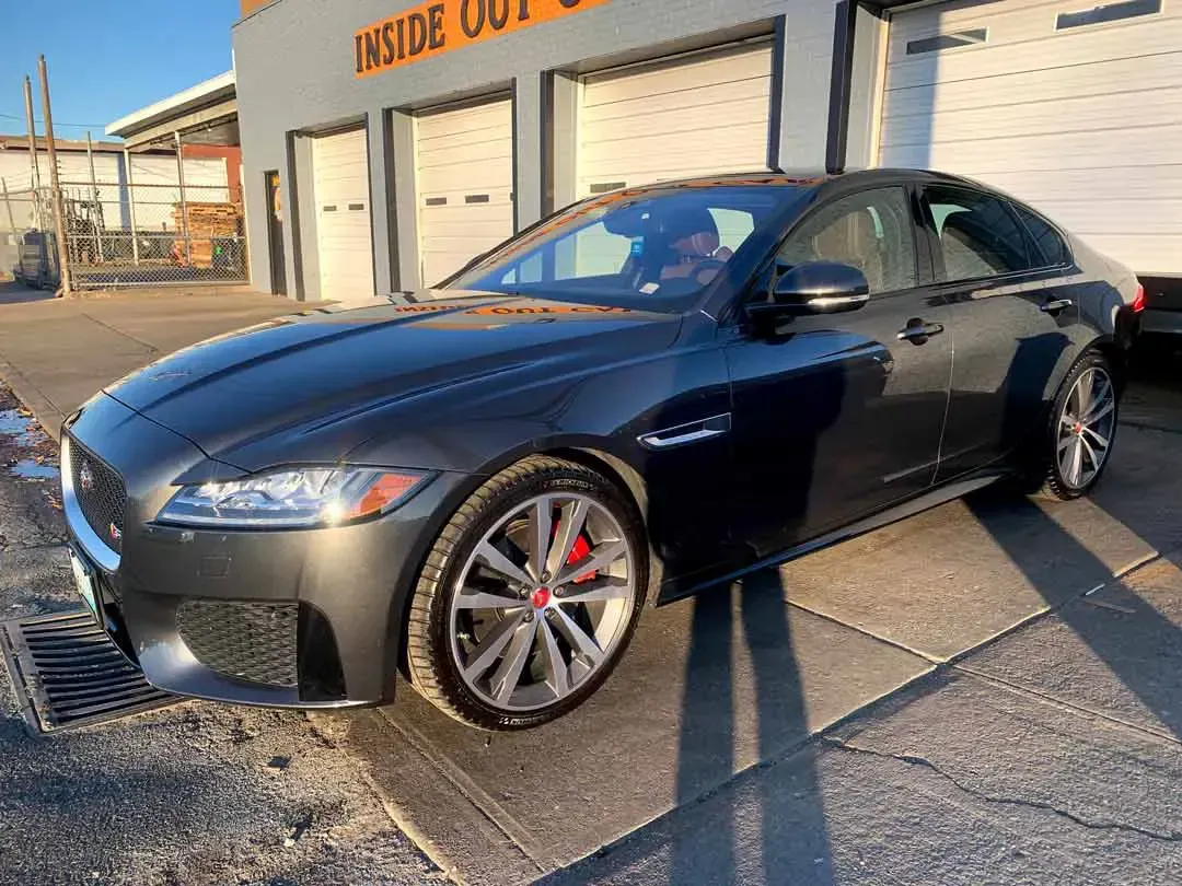 A black jaguar f type is parked in front of a garage.