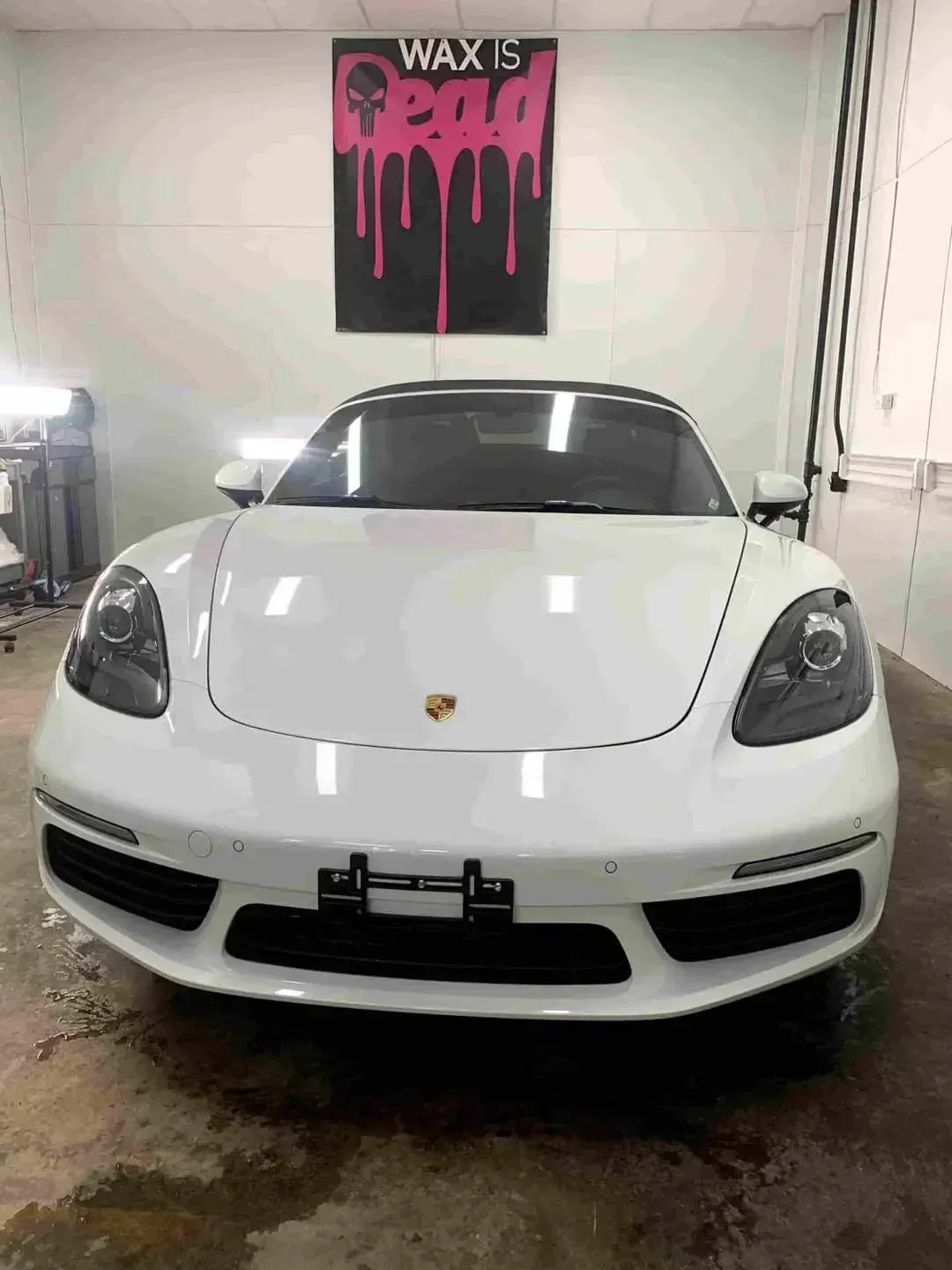 A white porsche boxster is parked in a garage.