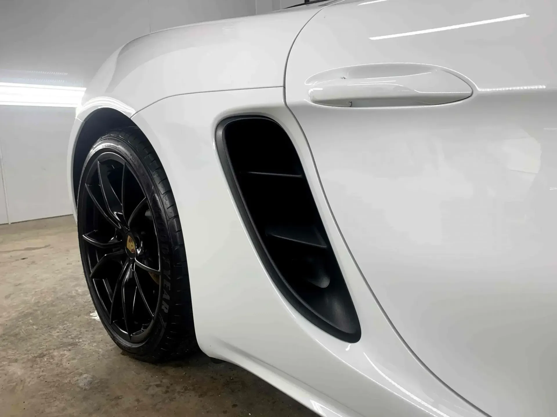 A white sports car with black wheels is parked in a garage.