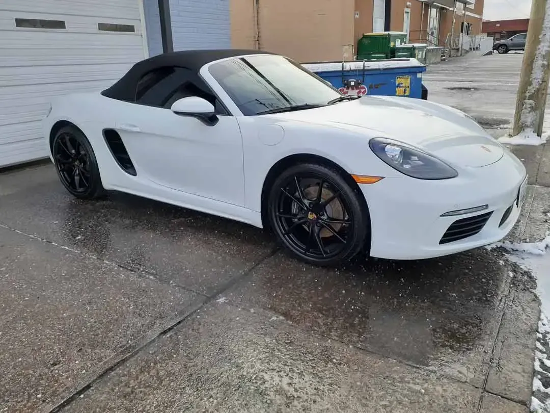 A white porsche boxster convertible is parked in front of a garage.