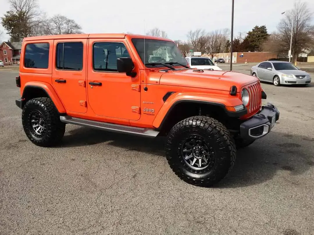 An orange jeep wrangler is parked in a parking lot.