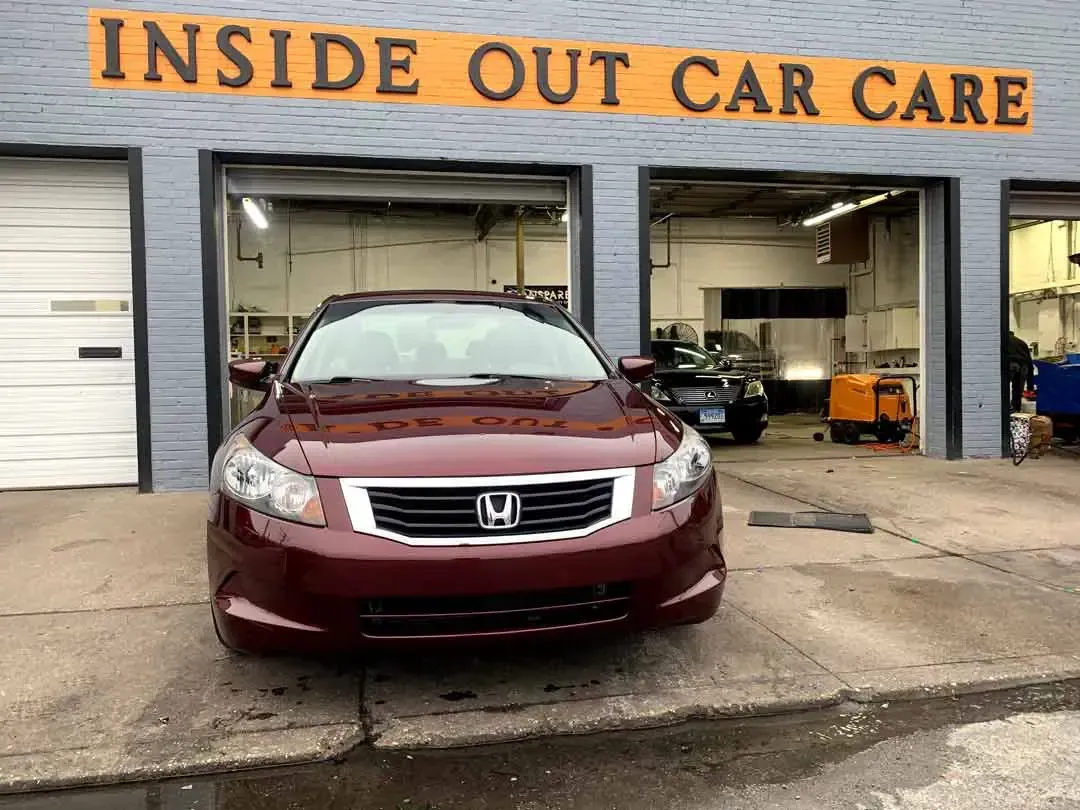 A red honda accord is parked in front of an inside out car care garage.