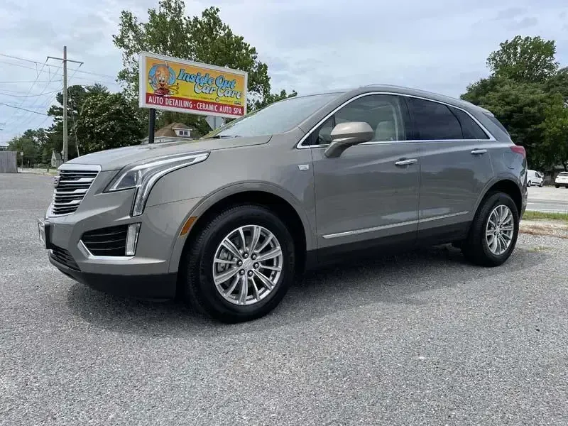 A silver cadillac escalade is parked in a parking lot in front of a car dealership.