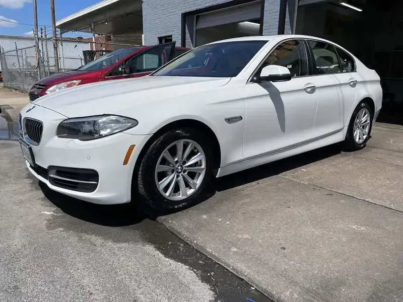 A white bmw 5 series is parked in front of a garage.